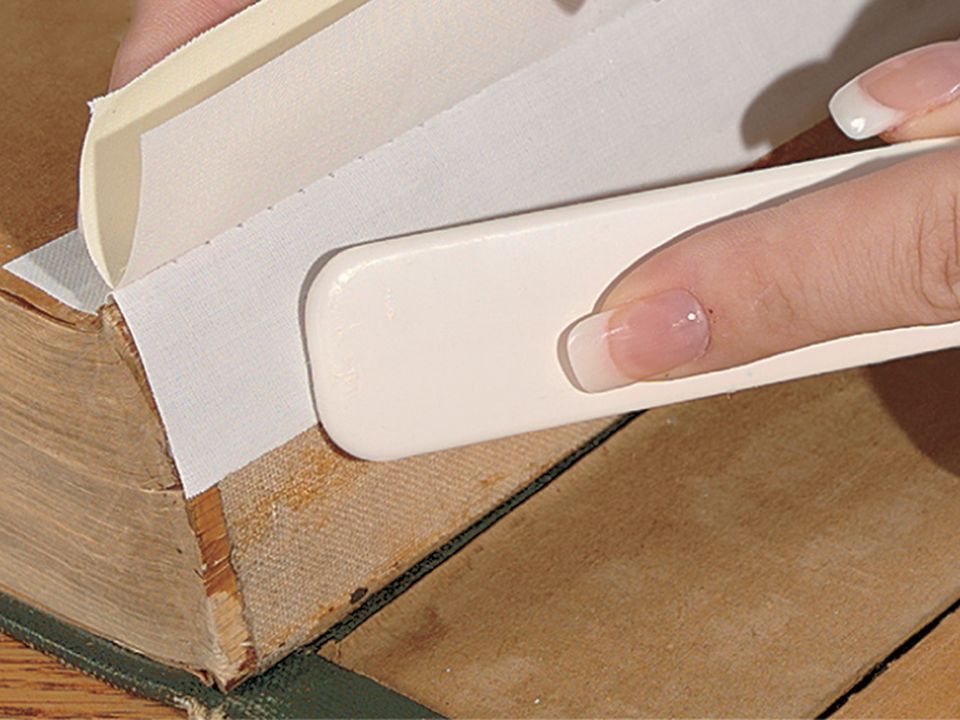 A hand creasing paper with a white bone folder