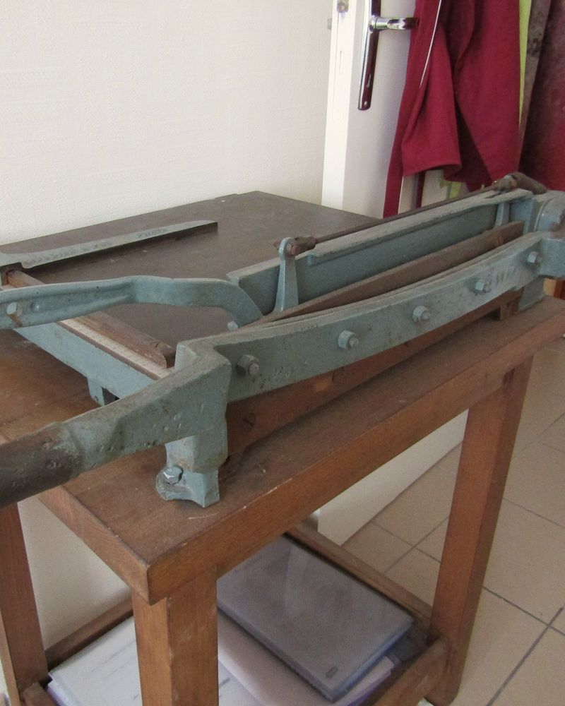An old cast-iron paper cutter on a wooden stand