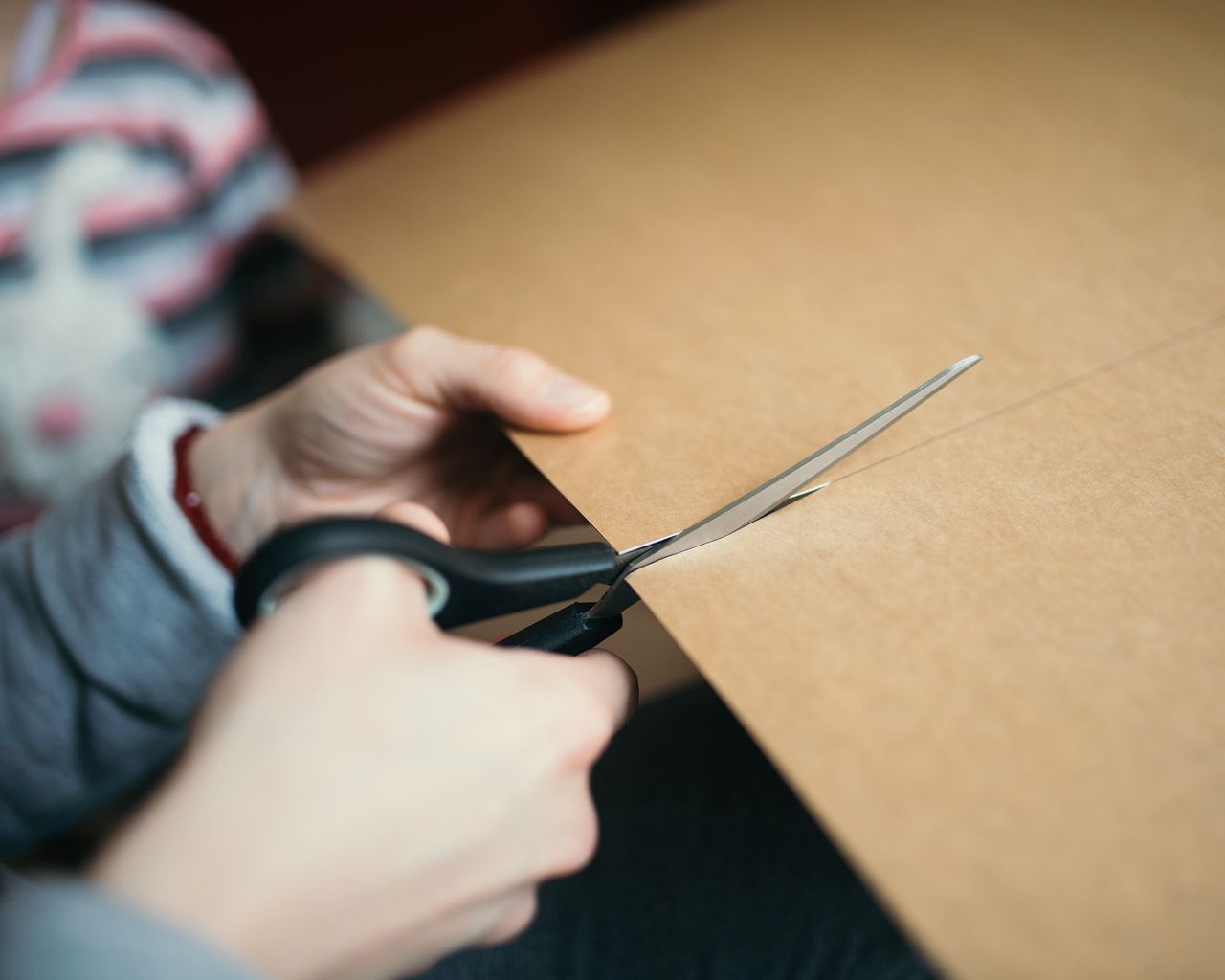 Hands cutting a sheet of brown card with scissors