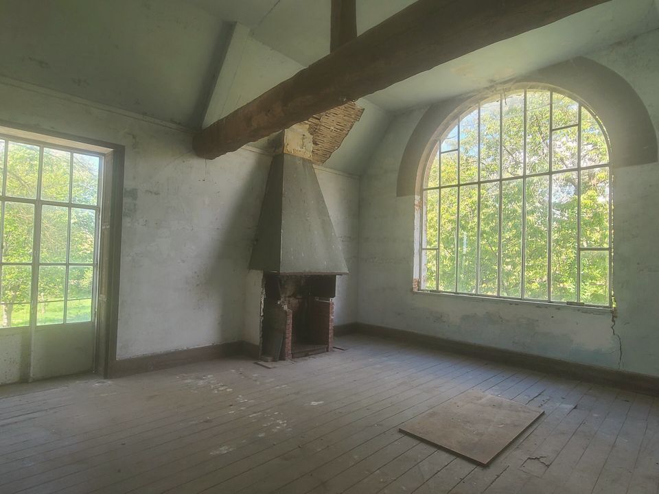 An empty studio room with a tall arched window and bare floorboards