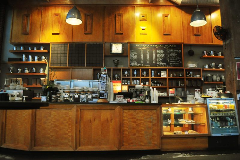 A cafe counter with wooden cabinets and shelves of cups and coffee gear under warm pendant lights