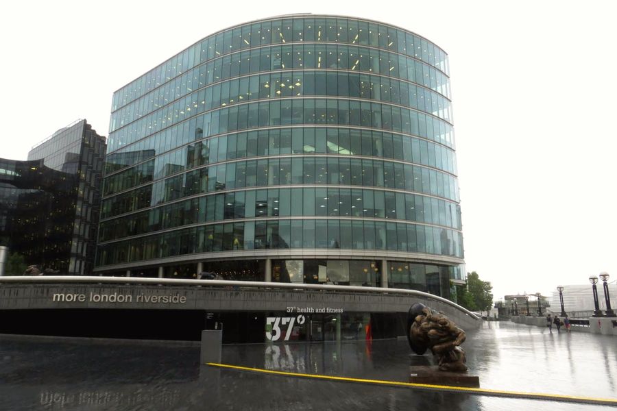 Curved glass office building rising above a paved riverside walk