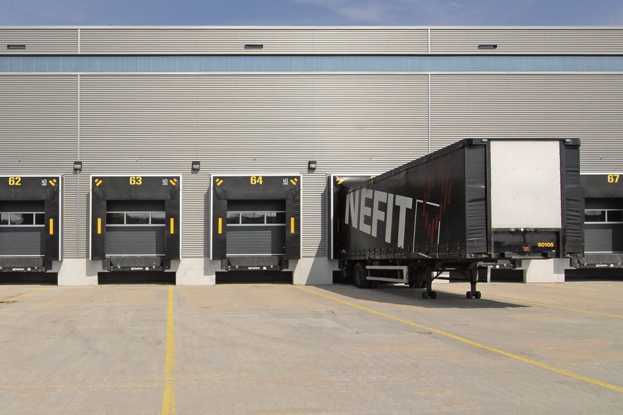 Grey-clad warehouse wall with a row of loading dock doors and a lorry trailer backed onto one of them