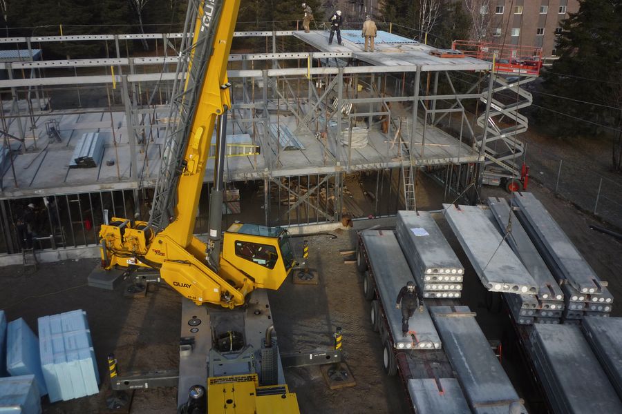 A yellow mobile crane beside a part-built steel frame, with stacks of steel beams laid out on the ground