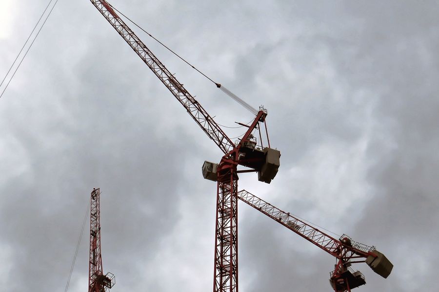 Two red tower cranes against a grey, cloudy sky