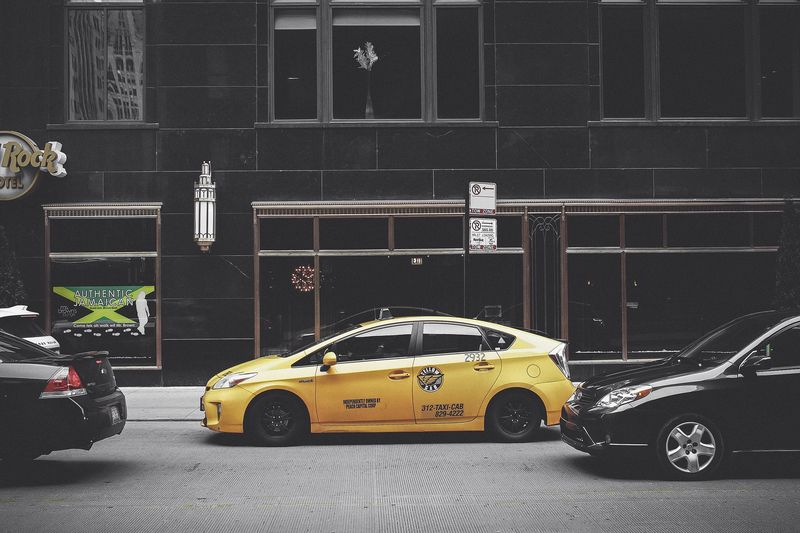 A yellow cab parked between dark cars on a city street