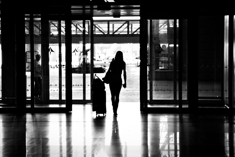 A traveller pulling a case through an airport hall, in silhouette