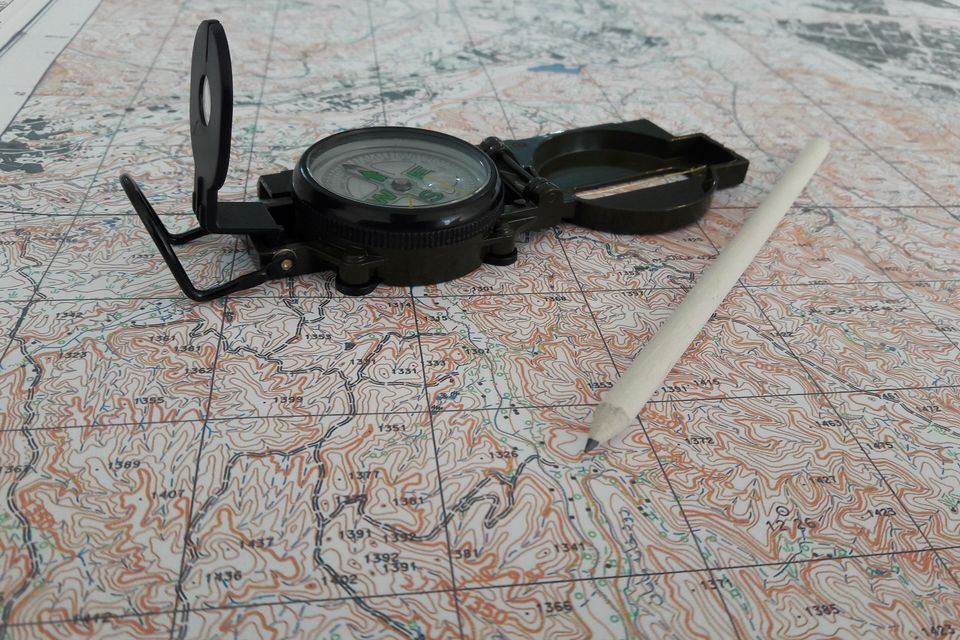 A sighting compass and a pencil lying on a topographic map