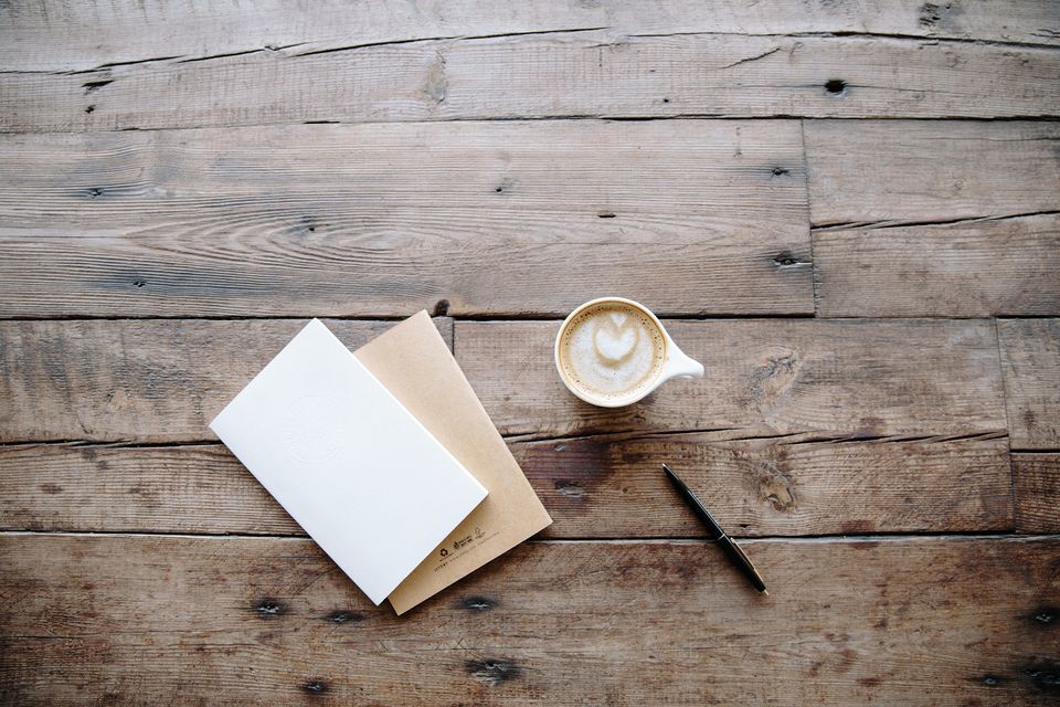 Notebooks, a pencil and a small cup of coffee on weathered wooden boards