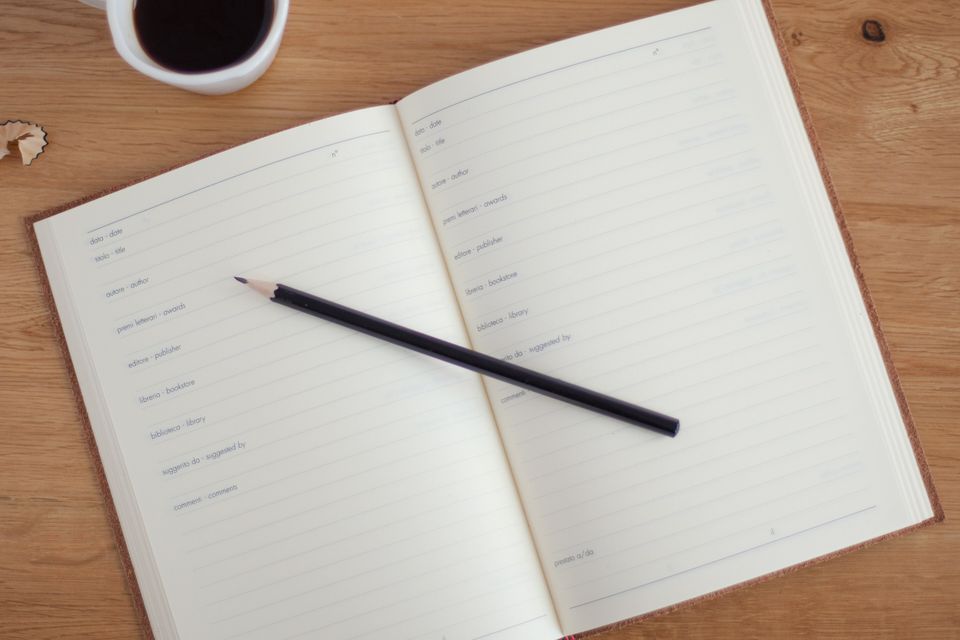 An open notebook with a pen and a cup of coffee on a wooden table