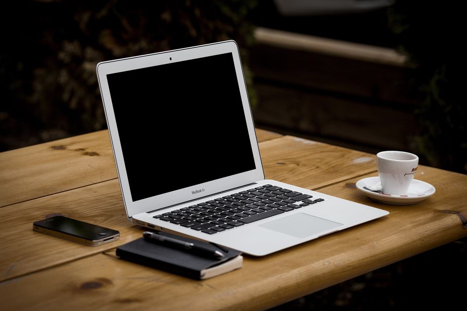 An open laptop on a wooden table beside a cup of coffee and a phone