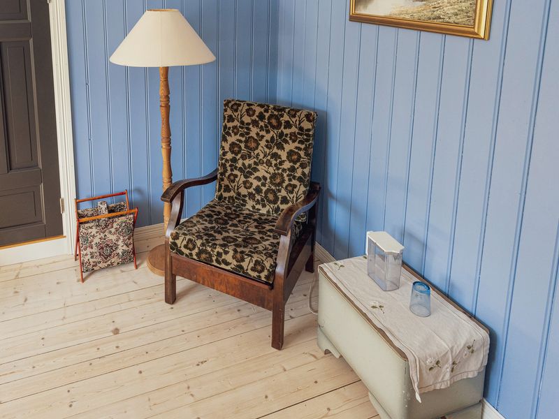 A reading corner with a patterned armchair, a standard lamp and a small table against blue wooden walls