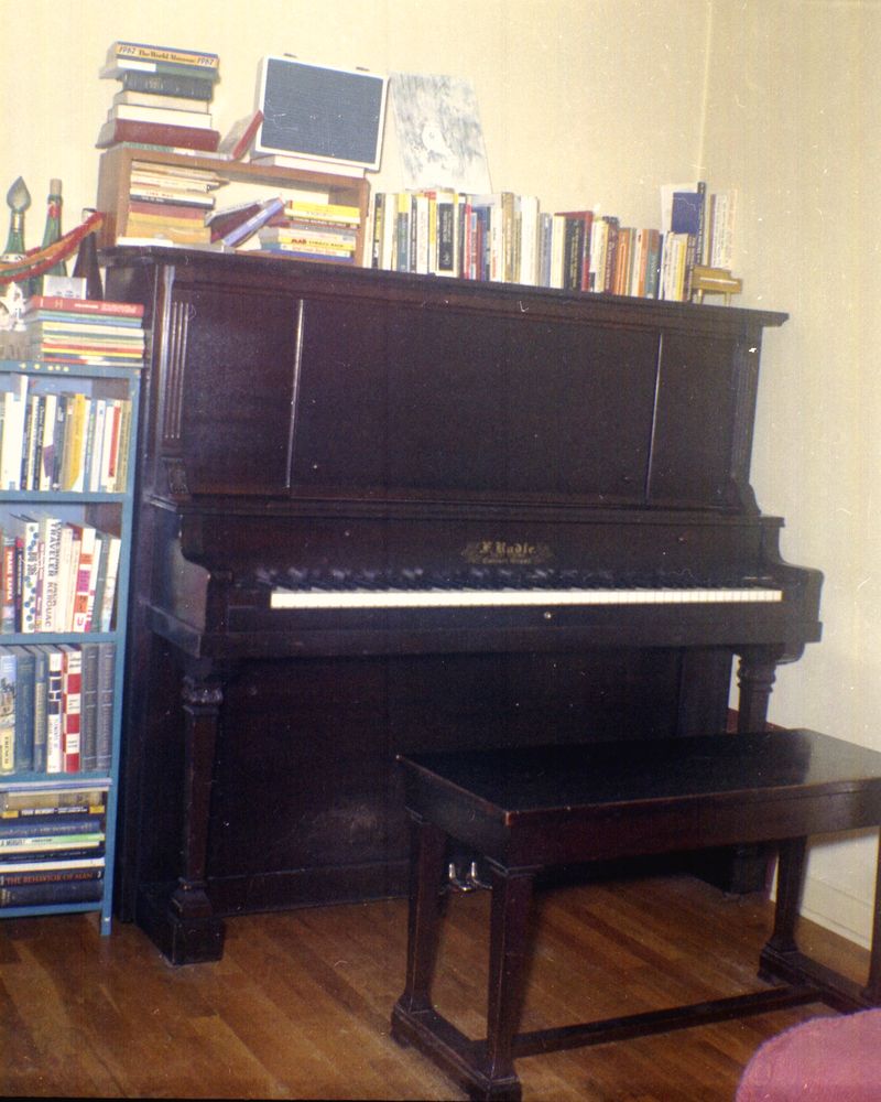 An upright piano and bench beside full bookshelves