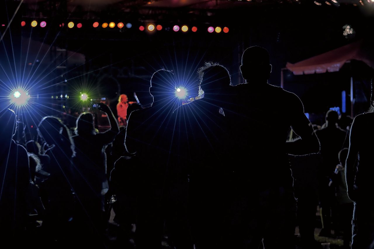 Silhouettes of a crowd in front of a stage lit blue and white