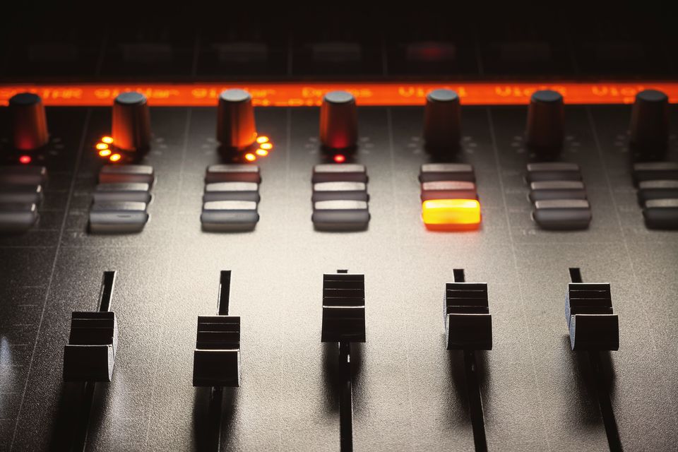 Faders on a mixing console, lit amber in a dark studio