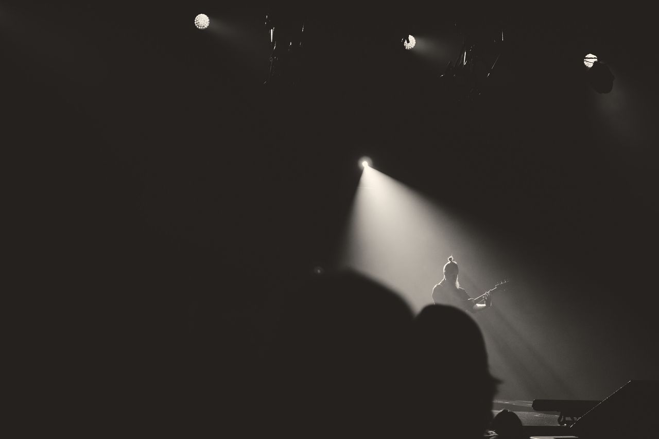 A lone guitarist lit by a single white beam on a dark stage