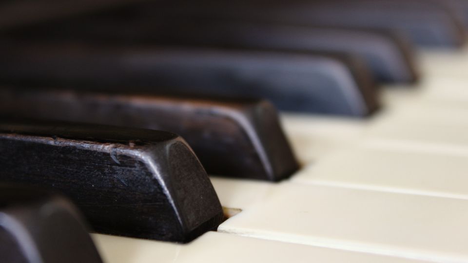 A black piano key in close-up, the rest of the keyboard falling into shadow