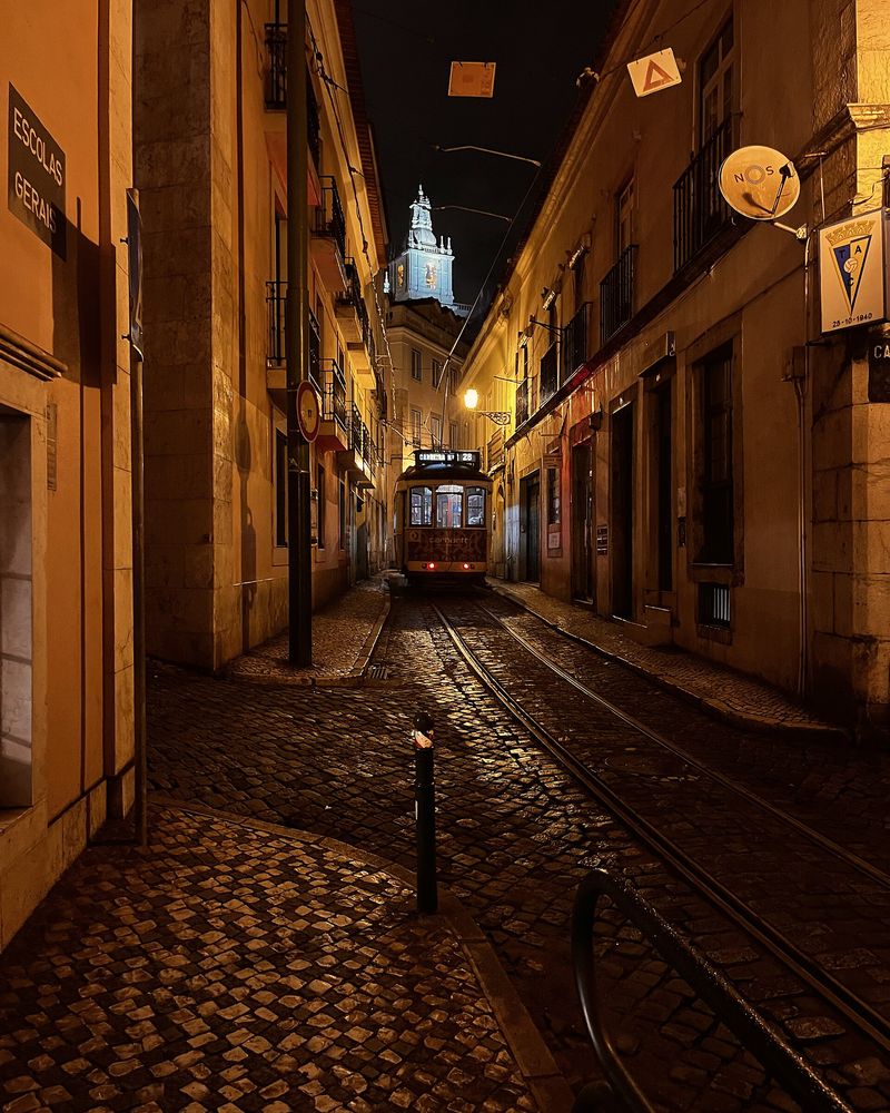 A narrow Lisbon street at night, tram rails shining on the cobbles