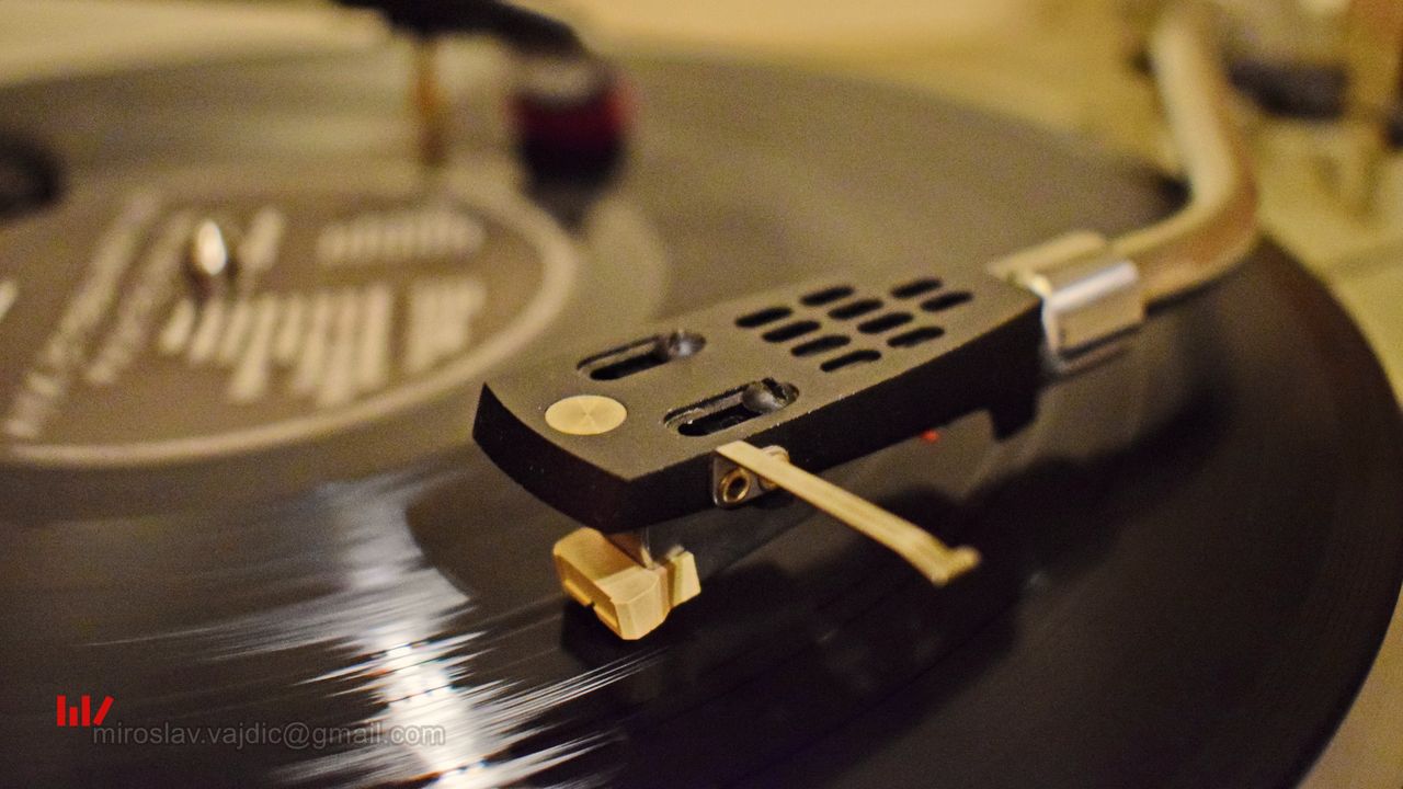 A turntable tonearm resting over a spinning black record