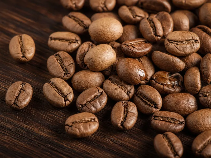 Roasted coffee beans piled on a dark wooden surface.