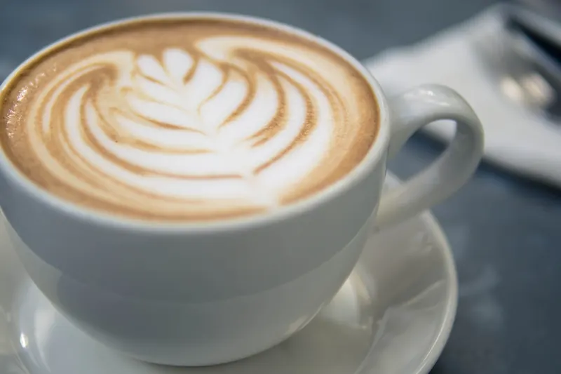 A cappuccino with a leaf of latte art in a white cup and saucer.