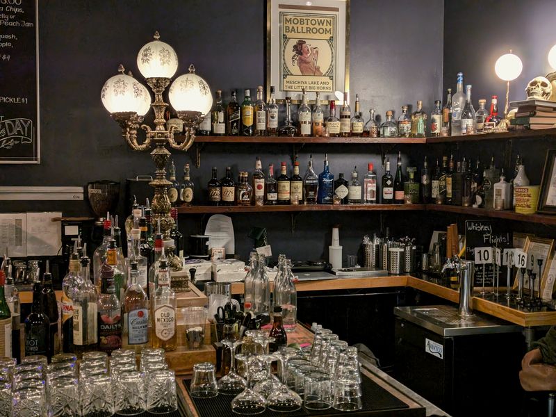 A bar with shelves of bottles, glass lamps and stacked glasses