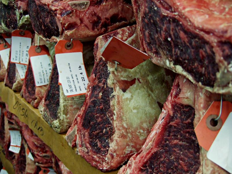 Large cuts of beef dry-ageing on shelves, each with a paper tag
