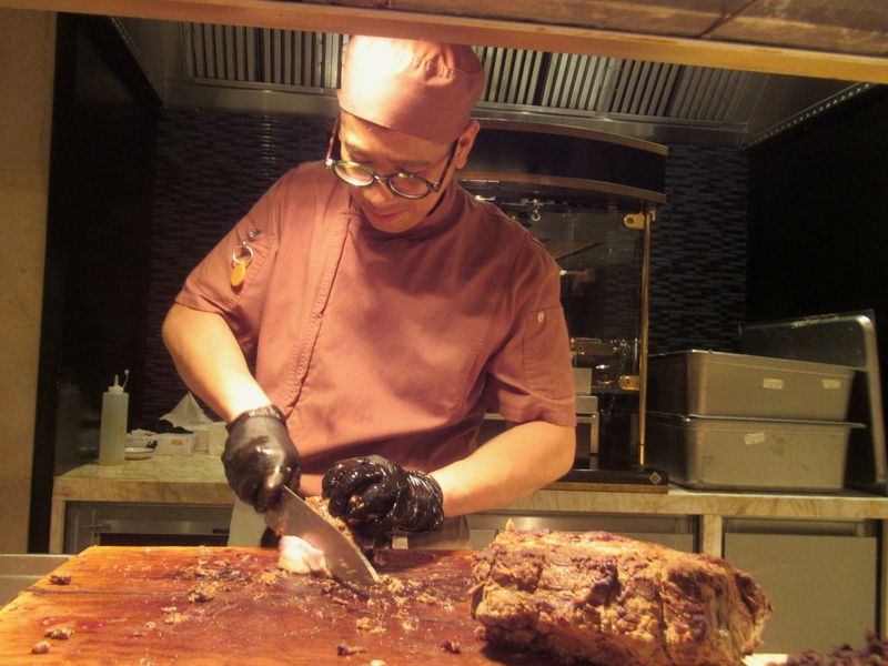 A cook in an apron and gloves carving a roast at a board
