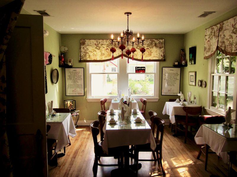 A small dining room with laid tables, a chandelier and tall windows