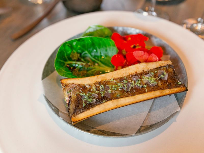 A split roasted marrow bone with cabbage leaves and orange nasturtium flowers on a plate