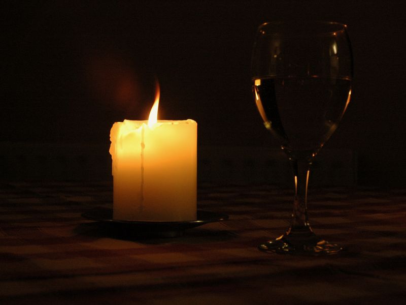 A lit candle and a wine glass on a table in a dark room