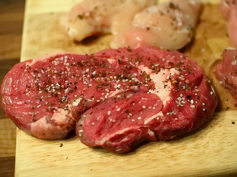 A raw seasoned ribeye steak on a wooden board