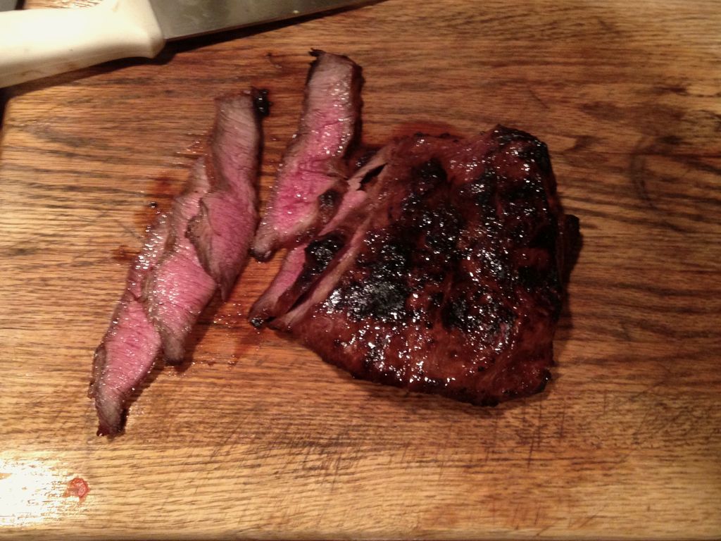 A seared steak, partly sliced to show a pink middle, on a wooden board