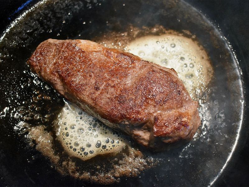 A steak searing in foaming butter in a black pan