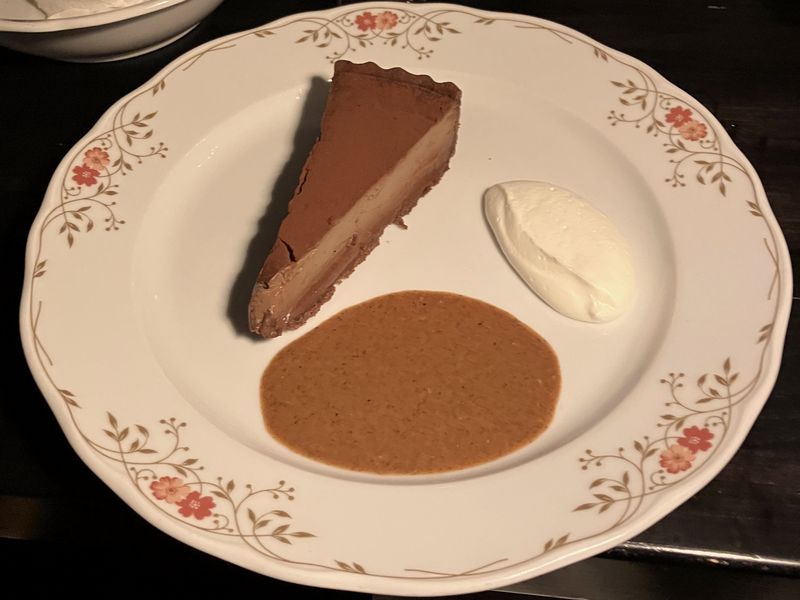 A slice of chocolate tart with a pool of sauce on a floral plate
