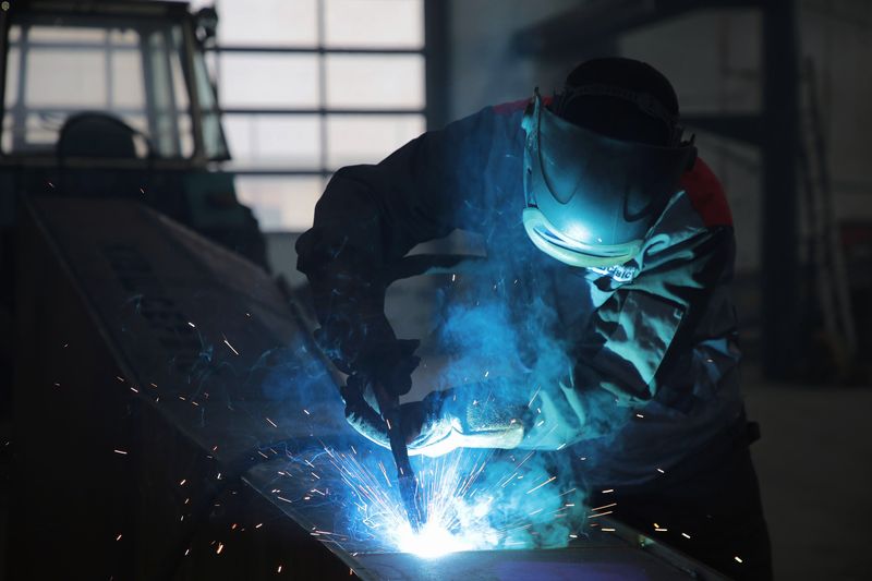 A welder bent over a glowing joint in a fabrication shop