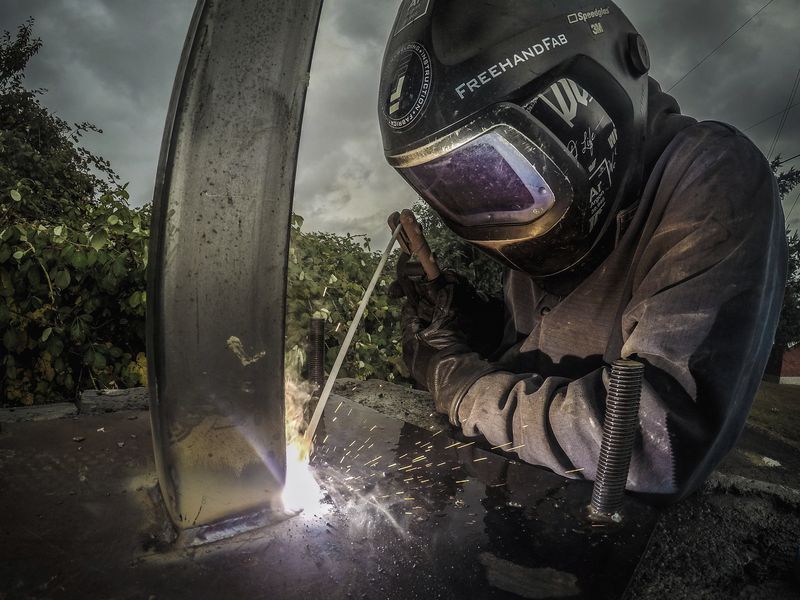 A welder in a mask welding a curved steel piece
