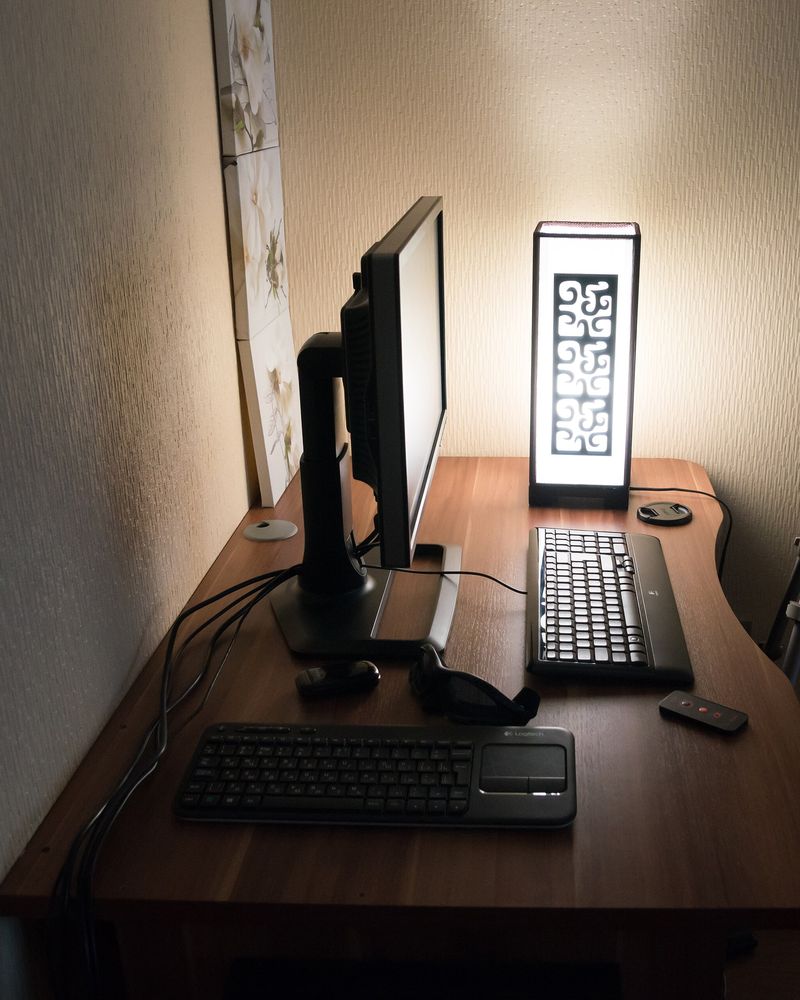 A small editing desk in a dark room, a monitor, keyboard and lamp, a tripod beside it