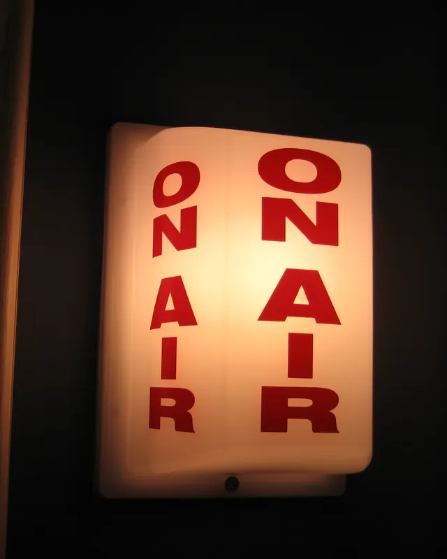 A lit “On Air” sign glowing red and white on a dark studio wall