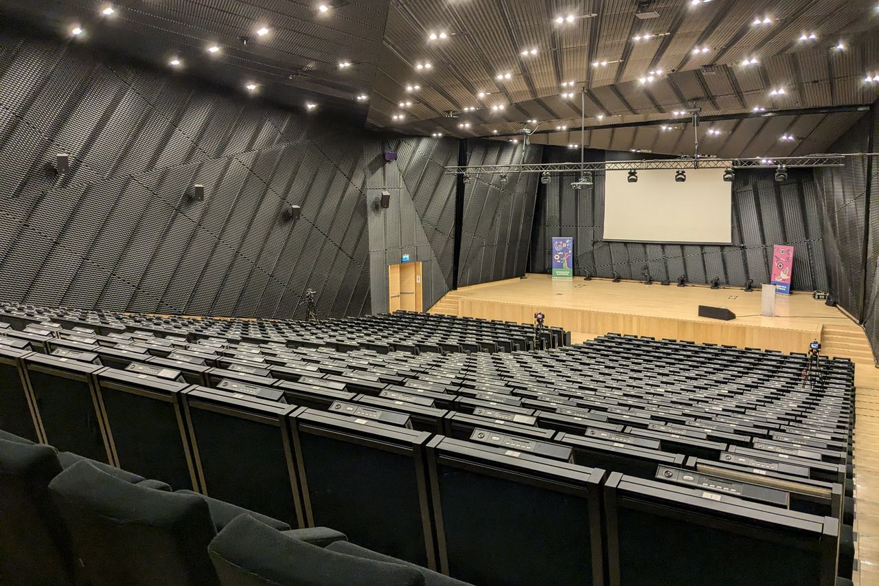 An empty raked auditorium with dark seats, ceiling spotlights and a small stage
