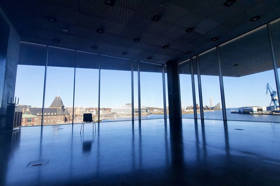 An empty room with floor-to-ceiling windows looking out over a harbour