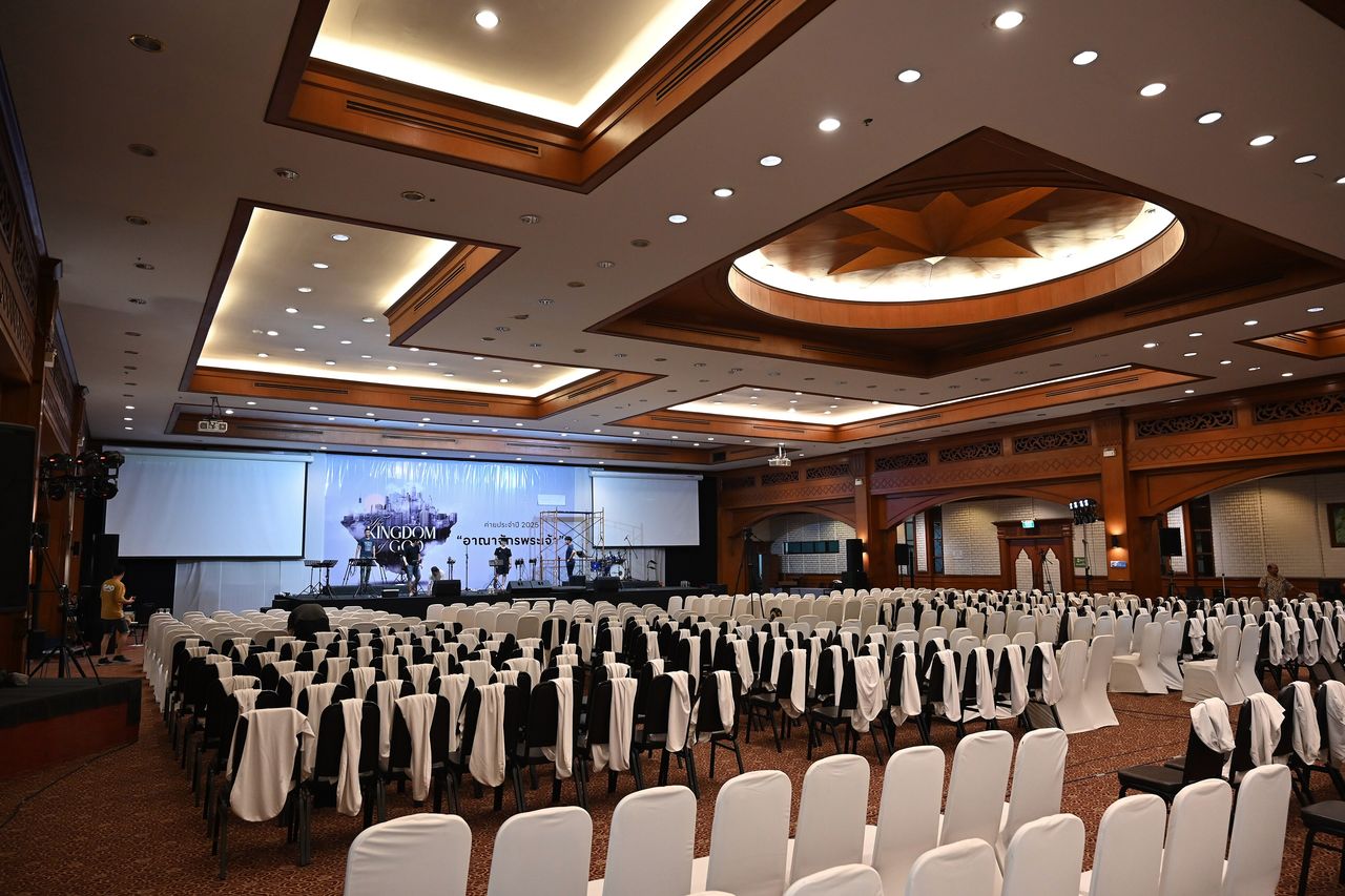 A large function room set with rows of white-covered chairs facing a stage and screens
