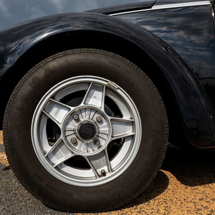 A silver alloy wheel under the curved black wing of a classic car