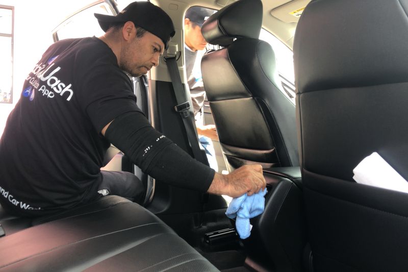 A man in a cap cleaning the seat of a car interior with a cloth