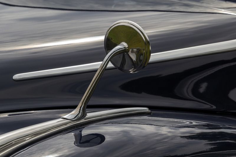A chrome wing mirror on the gloss black bonnet of a classic car