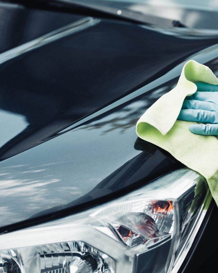A gloved hand wiping the bonnet of a black car with a yellow microfibre cloth