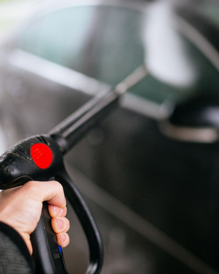 A hand holding a pressure washer lance against the door of a black car