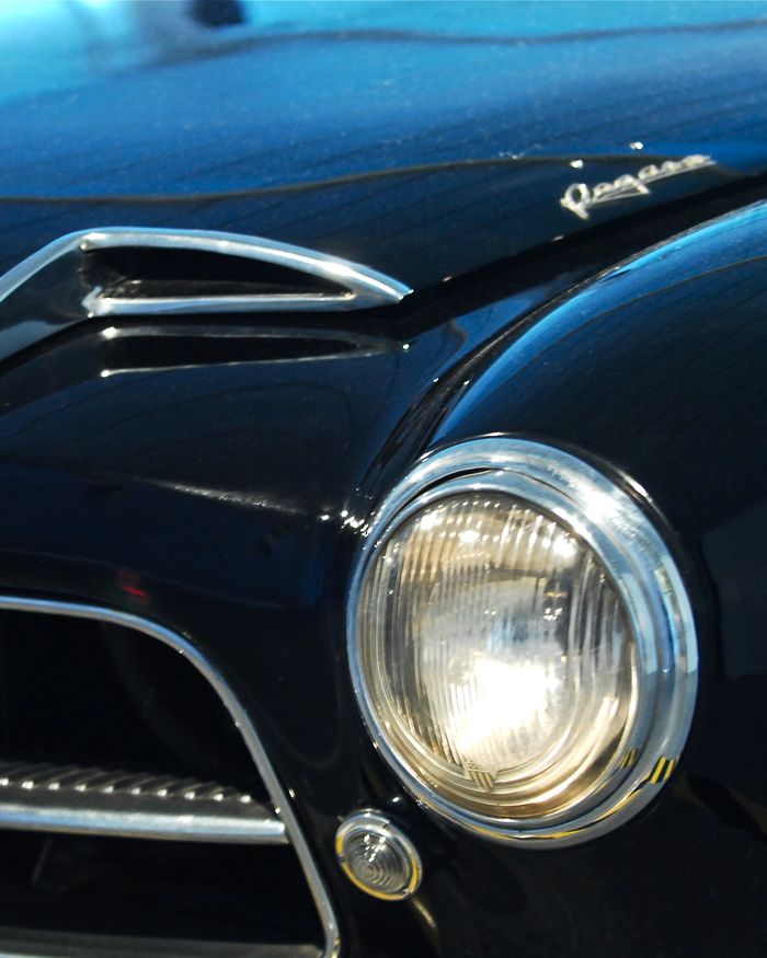 Close-up of the round headlamp and chrome trim of a dark blue classic car