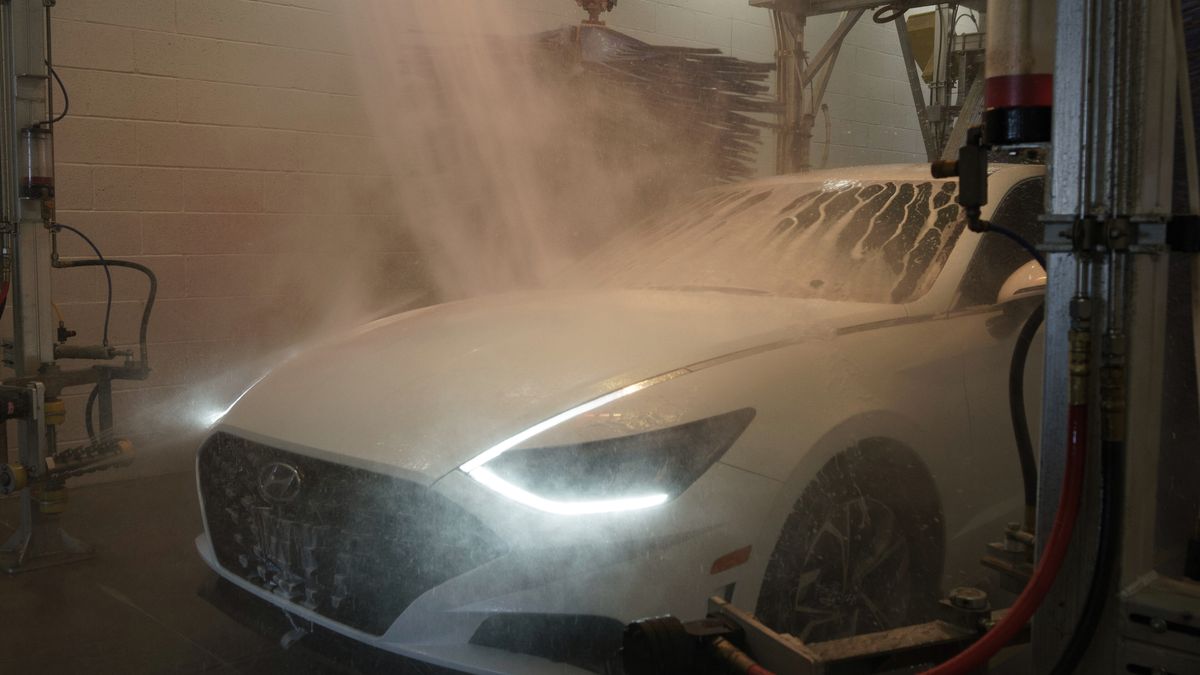 A white car under spray and mist in an automatic wash bay, headlights on