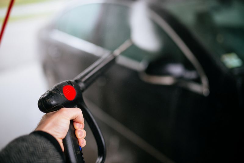 A hand holding a pressure washer lance against the door of a black car